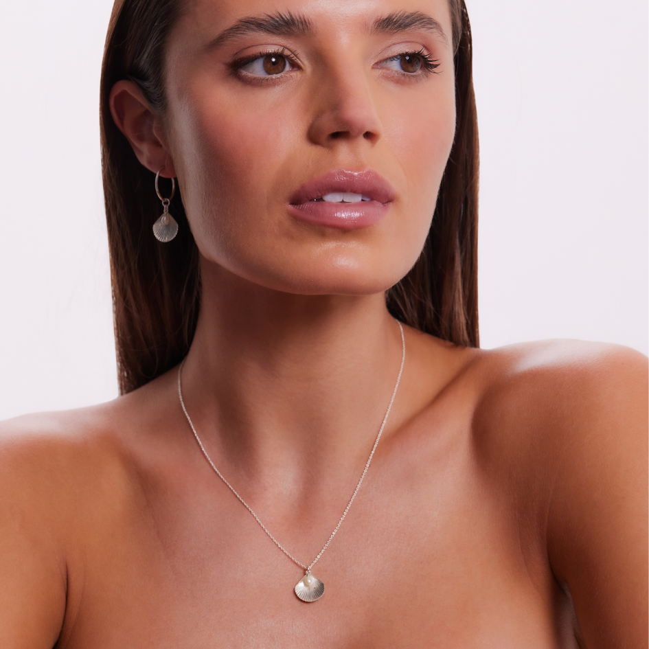 Woman wearing a silver necklace and earrings on a plain background