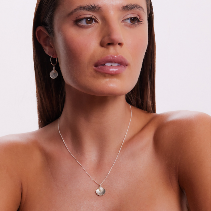 Woman wearing a silver necklace and earrings on a plain background